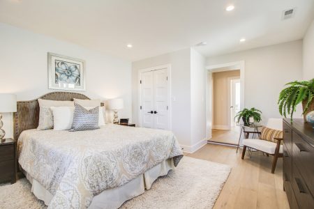 A master bedroom with a bed, a chair and white oak hardwood floors